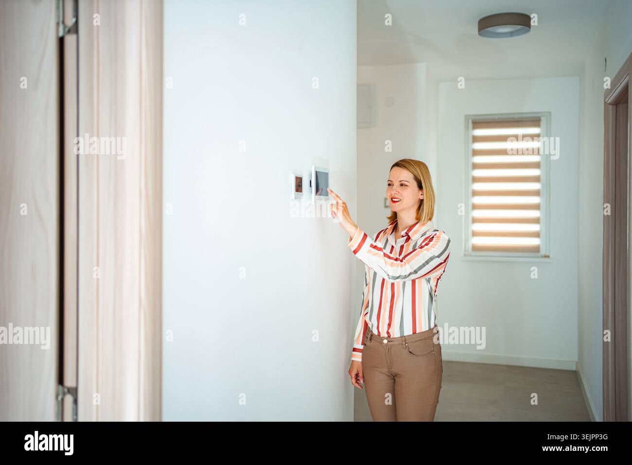Woman using smart home control panel in hallway Stock Photo
