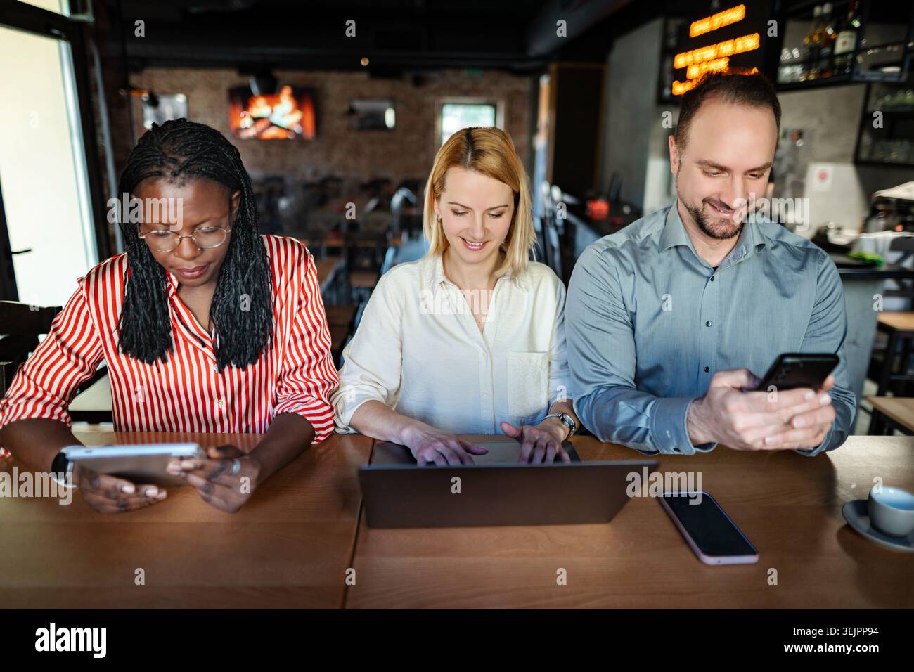 Diverse colleagues working together on digital devices in cafe Stock Photo