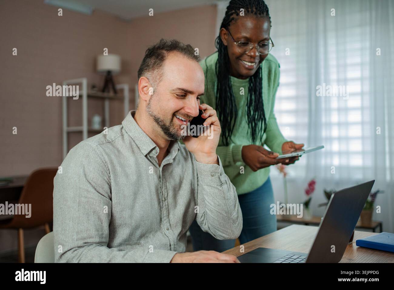 Multicultural couple working remotely from home, collaborating on digital devices Stock Photo