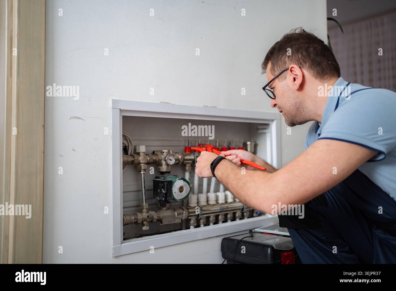 Plumber working on heating pipes inside building wall Stock Photo