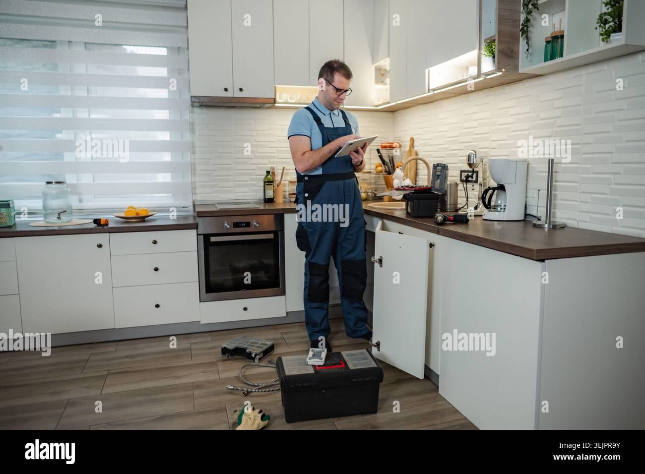 Plumber in overalls using tablet while repairing kitchen sink Stock Photo