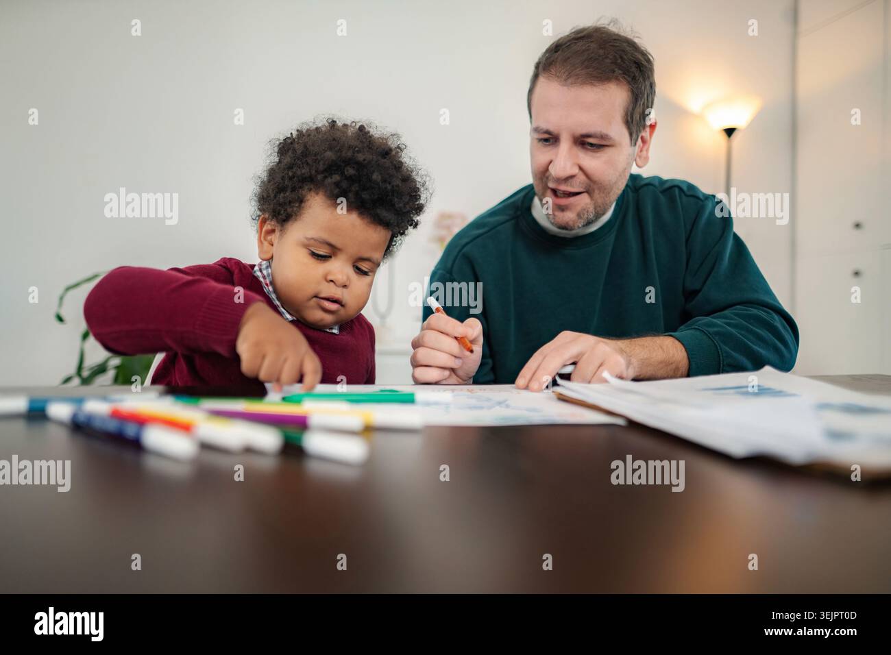 Father and son sitting at table drawing together Stock Photo