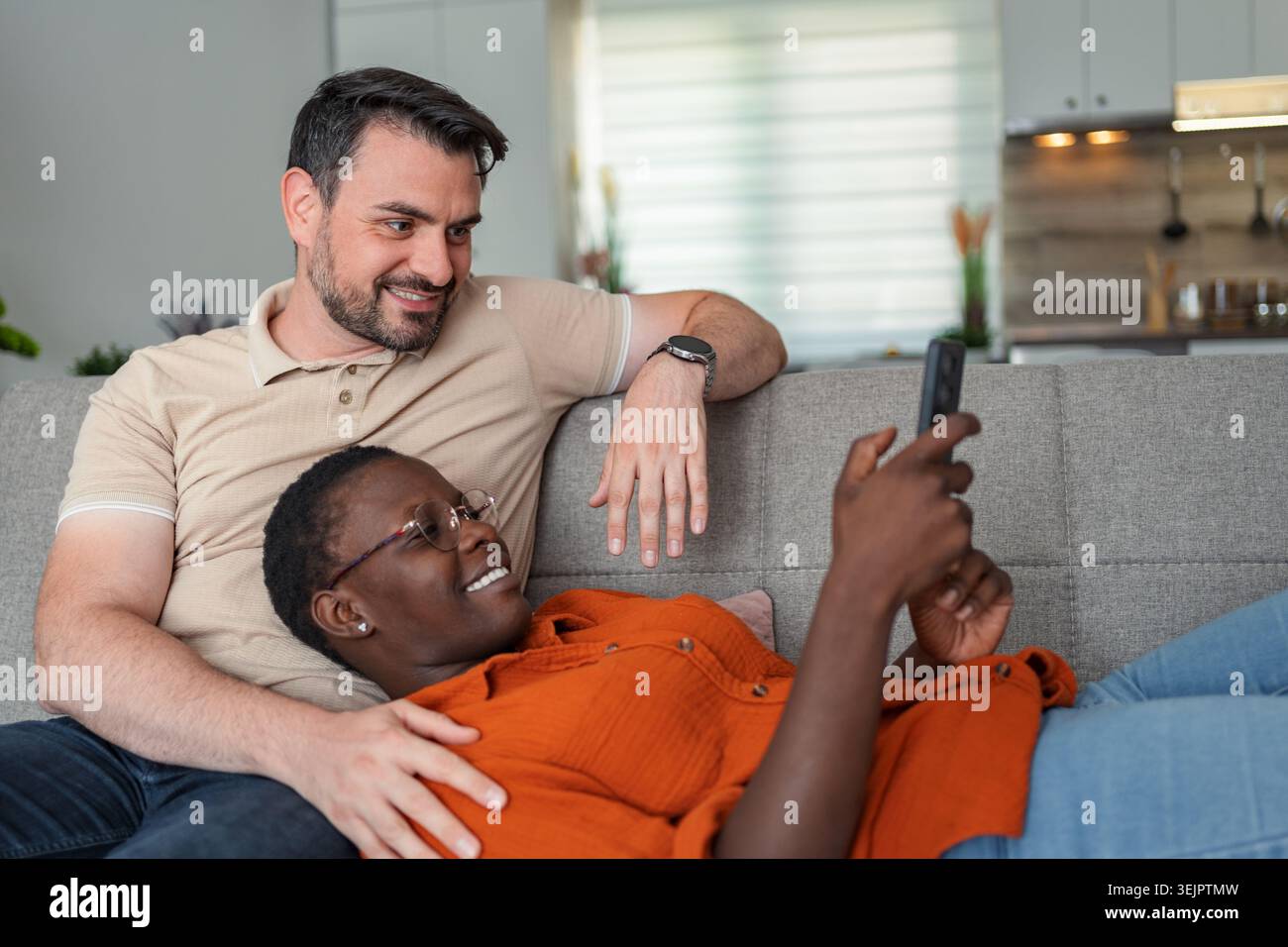 Interracial couple relaxing on sofa using smartphone at home Stock Photo