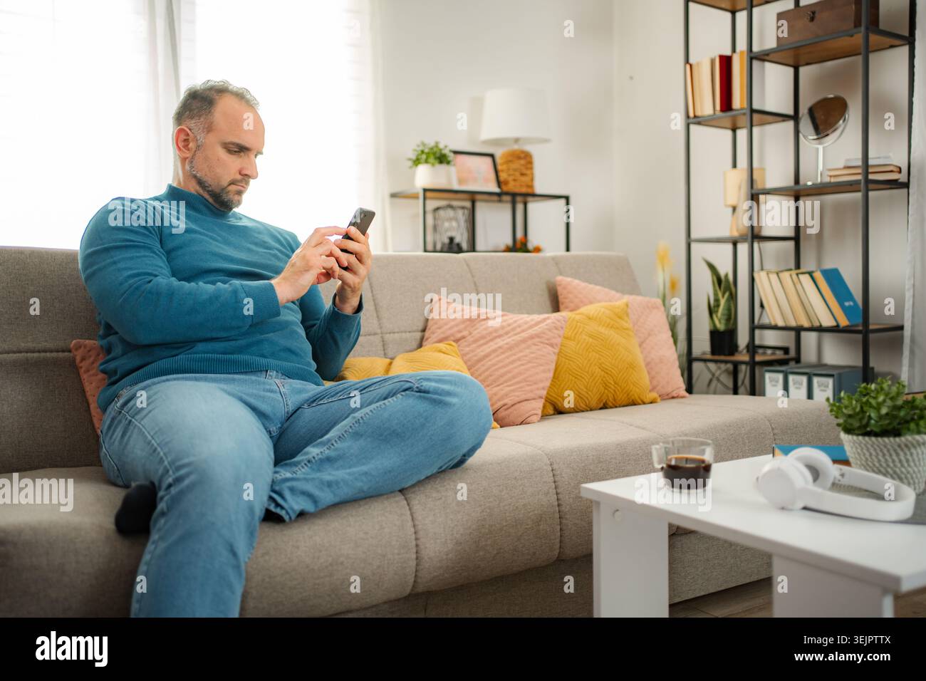 Man relaxing on sofa using smartphone at home Stock Photo