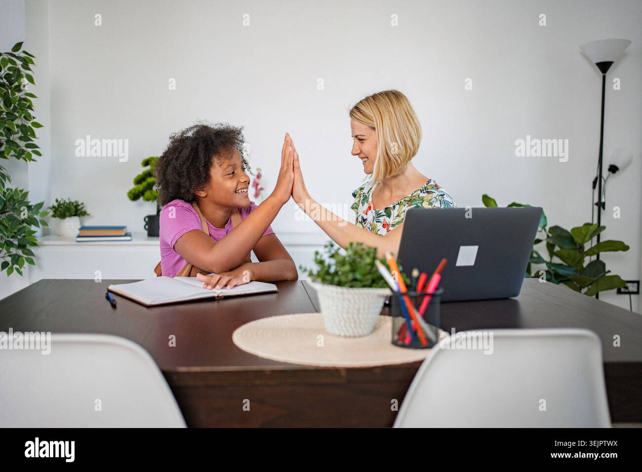 Mother and daughter giving high five while doing homework at home Stock Photo