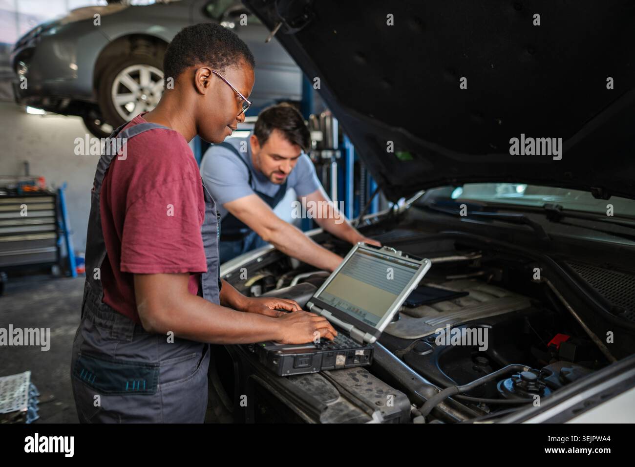 Mechanics using diagnostic software on laptop are examining car engine Stock Photo