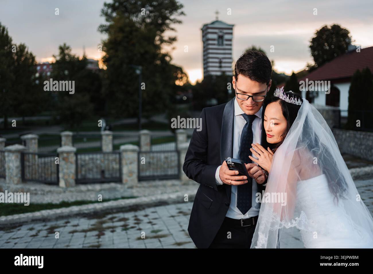 Interracial wedding couple looking at smartphone together outdoors Stock Photo