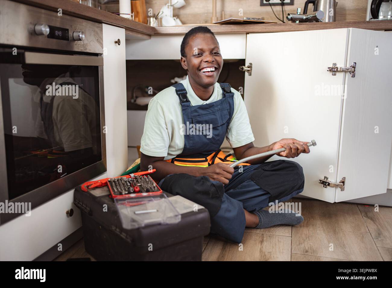 Smiling Plumber Fixing Sink Pipe in Kitchen Stock Photo