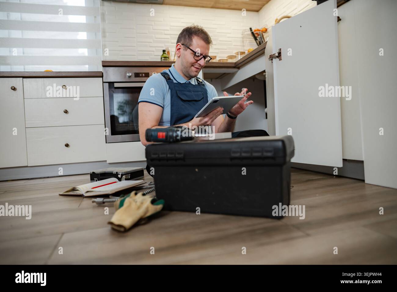 Handyman using digital tablet while repairing kitchen cabinet Stock Photo