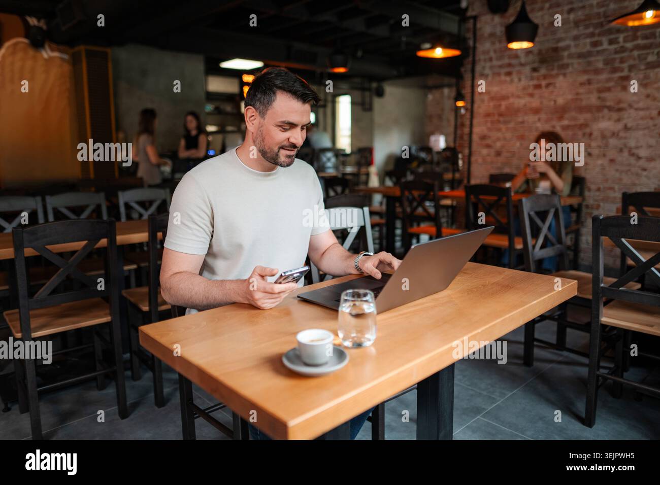 Freelancer working on laptop and using smartphone in cafe Stock Photo