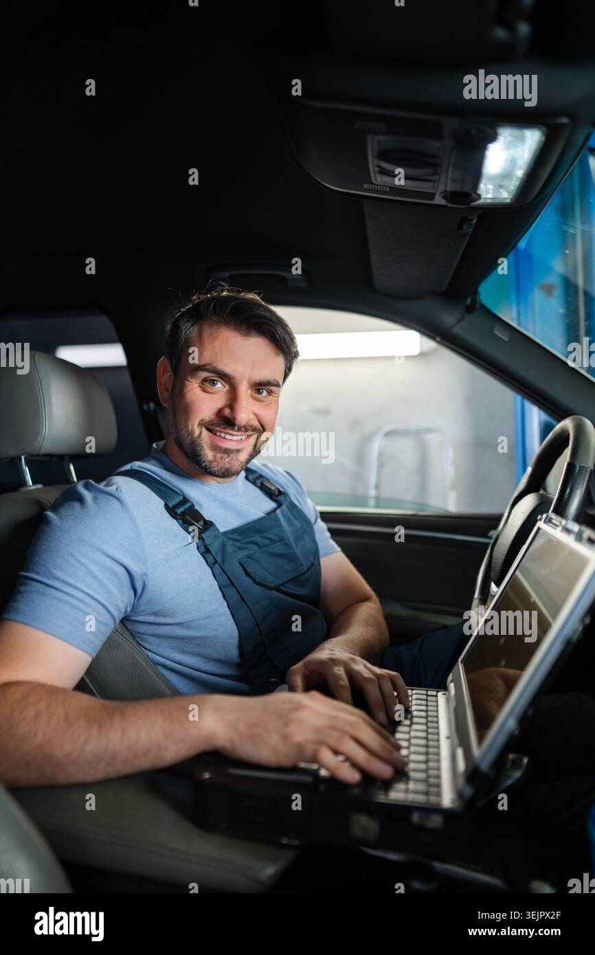 Smiling car mechanic using laptop for diagnostics inside a car Stock Photo