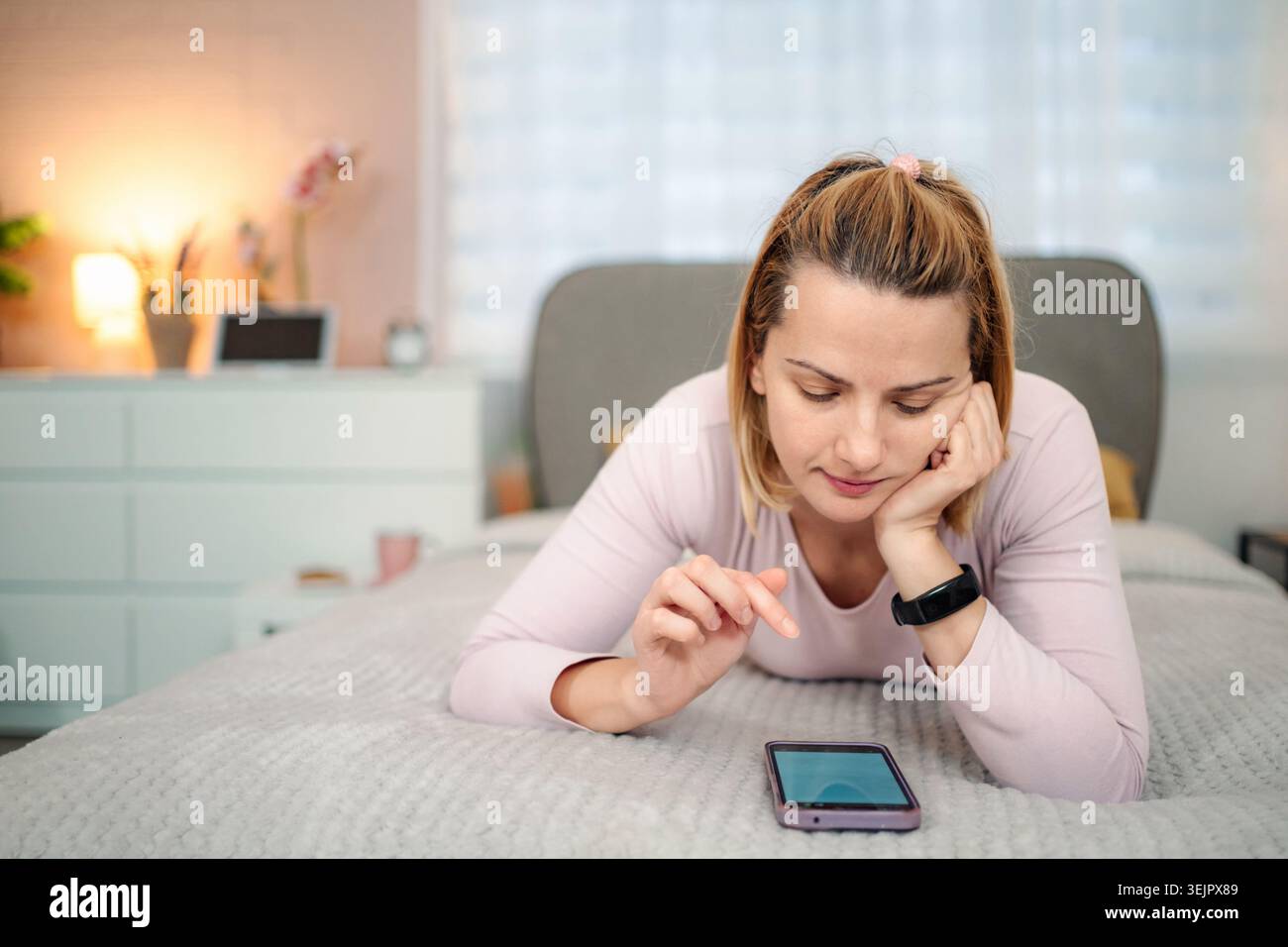 Woman lying on bed using smartphone at home Stock Photo
