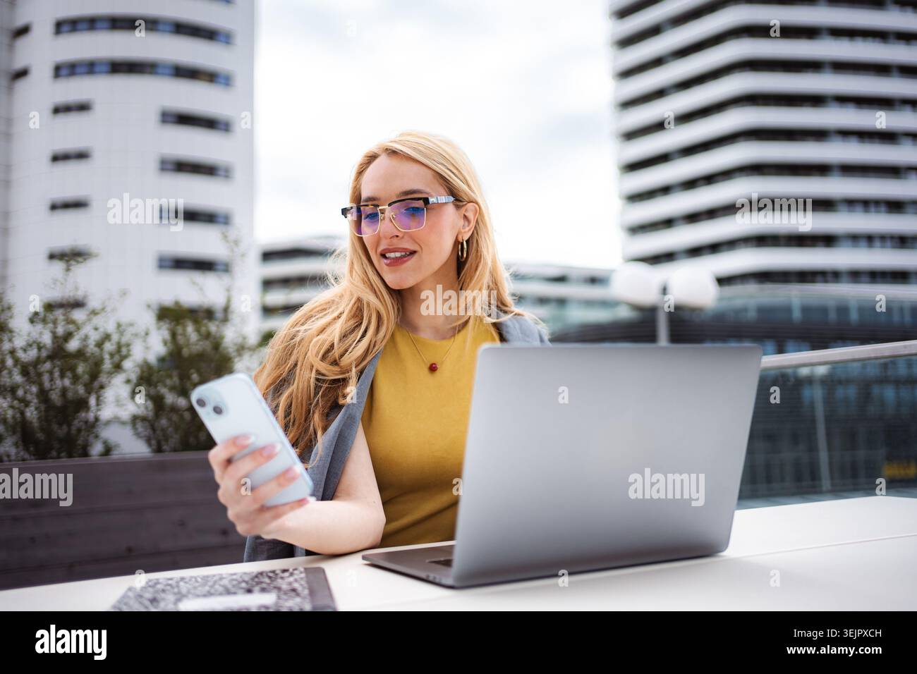 Businesswoman checking smartphone while working on laptop outdoors Stock Photo