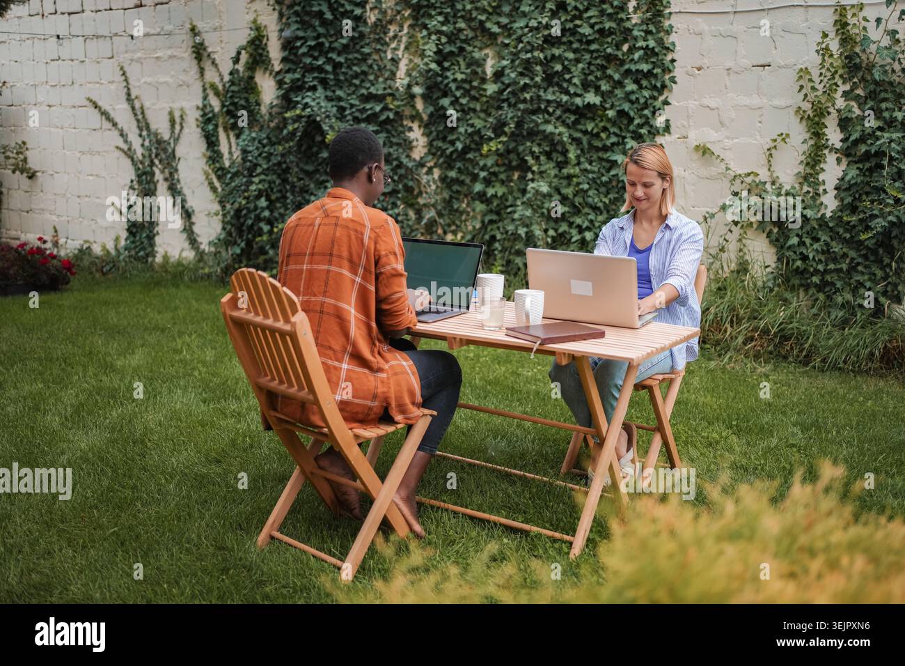 Two young professionals working remotely in a garden using laptops Stock Photo