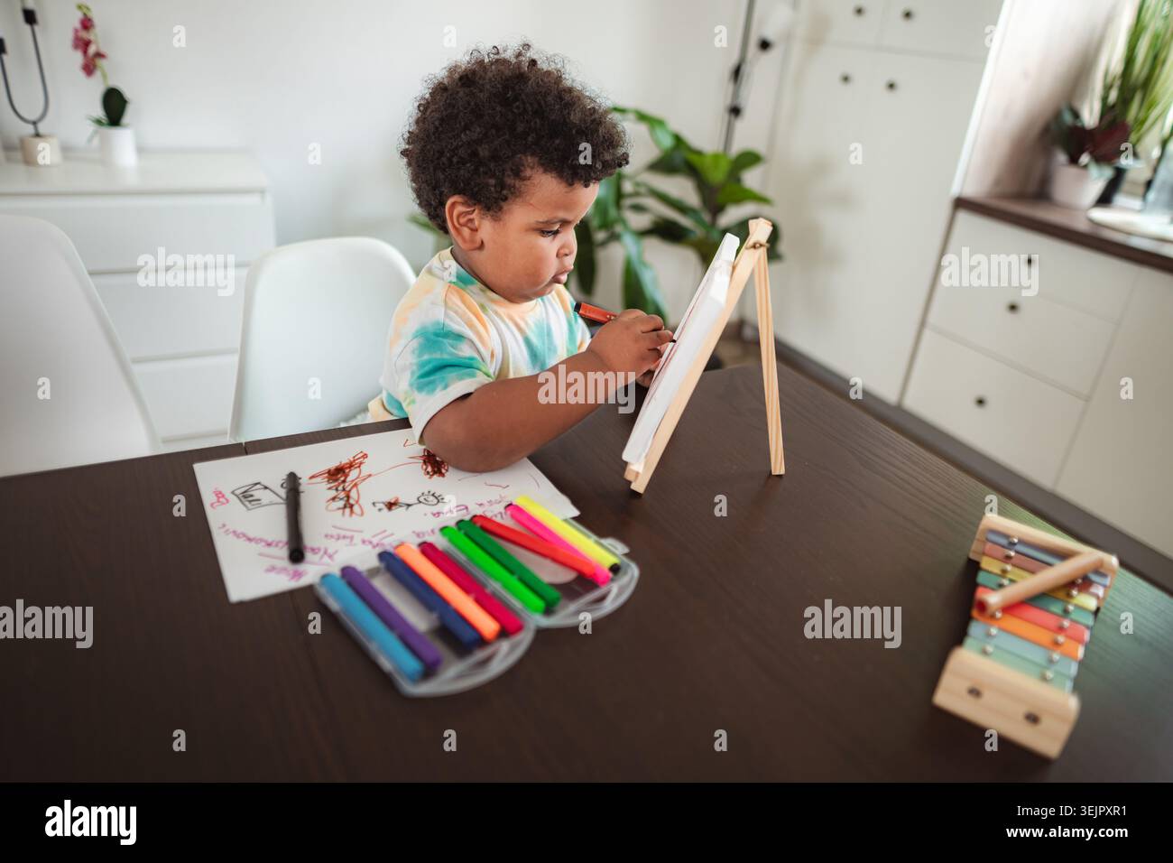 Toddler drawing on easel with colorful markers at home Stock Photo