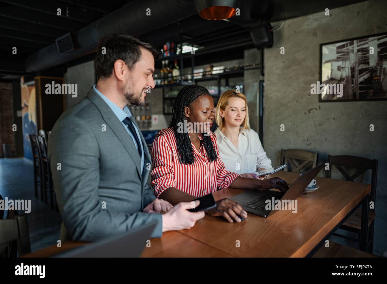 Three diverse colleagues discussing business strategy and using a laptop in a cafe Stock Photo