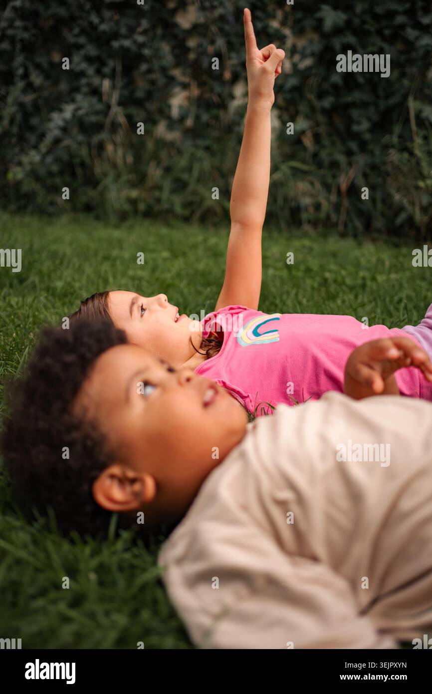 Children lying on grass pointing at sky exploring Stock Photo