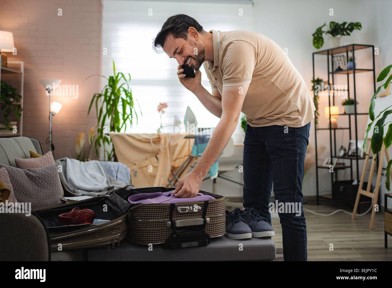 Man talking on the phone while packing suitcase at home Stock Photo