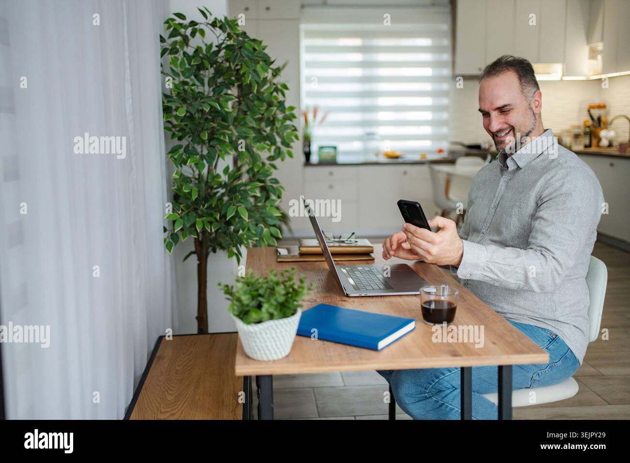 Freelance man working from home using laptop and smartphone Stock Photo