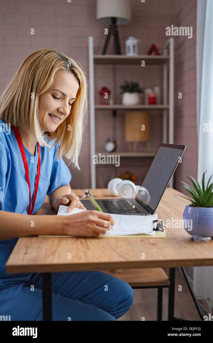 Female Doctor Working From Home Taking Notes and Smiling Stock Photo