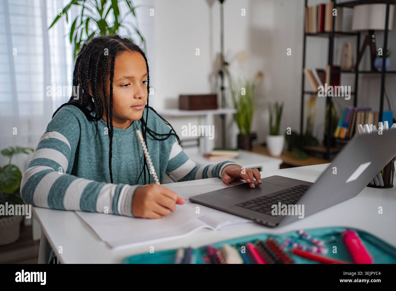Girl studying homework at desk using laptop for remote learning Stock Photo