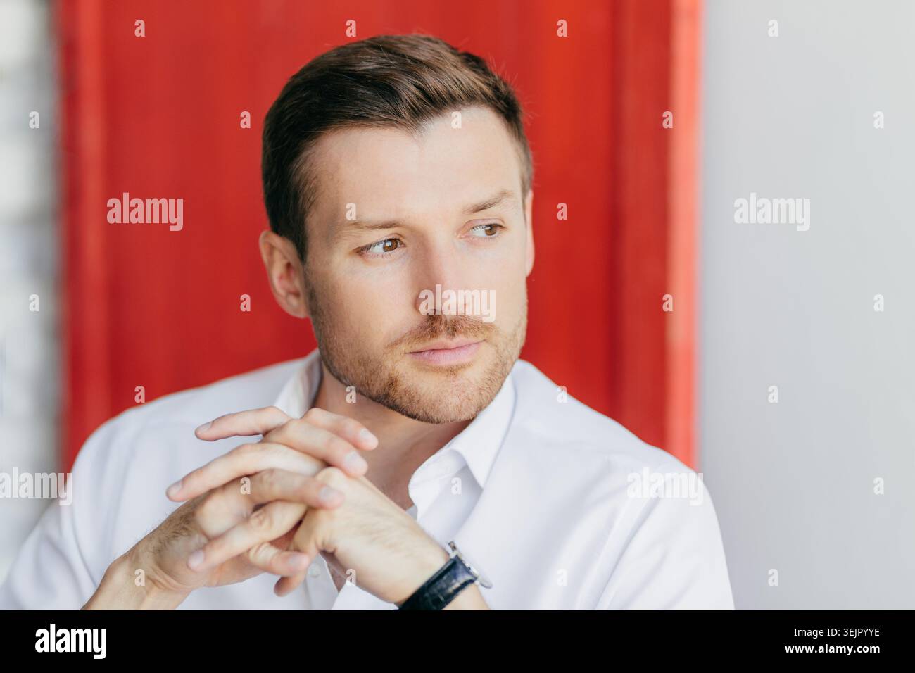 Thoughtful businessman portrait with hands clasped against red background looking away professional close up Stock Photo