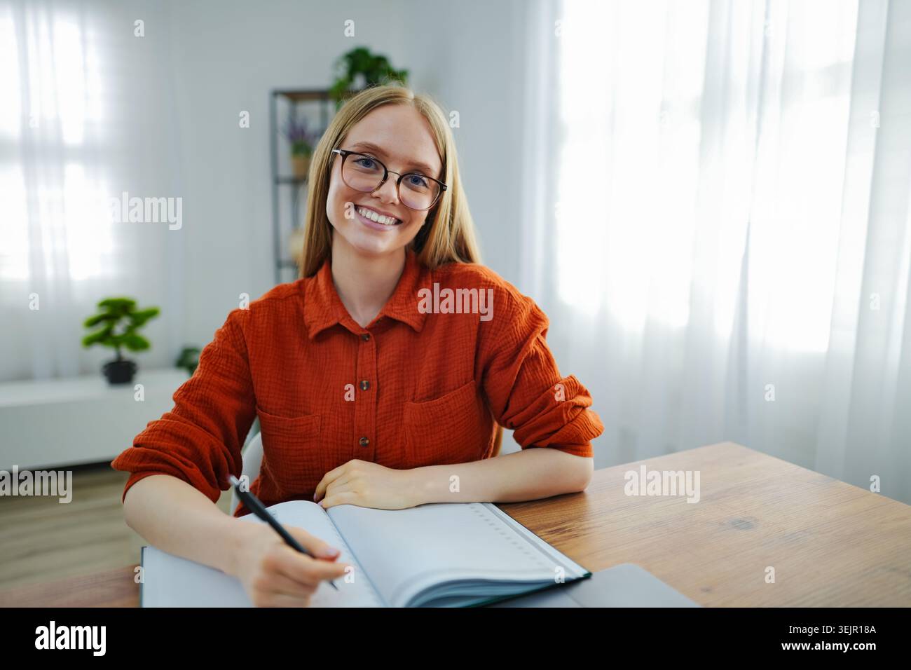 Woman smiling while writing in a notebook in a bright room Stock Photo