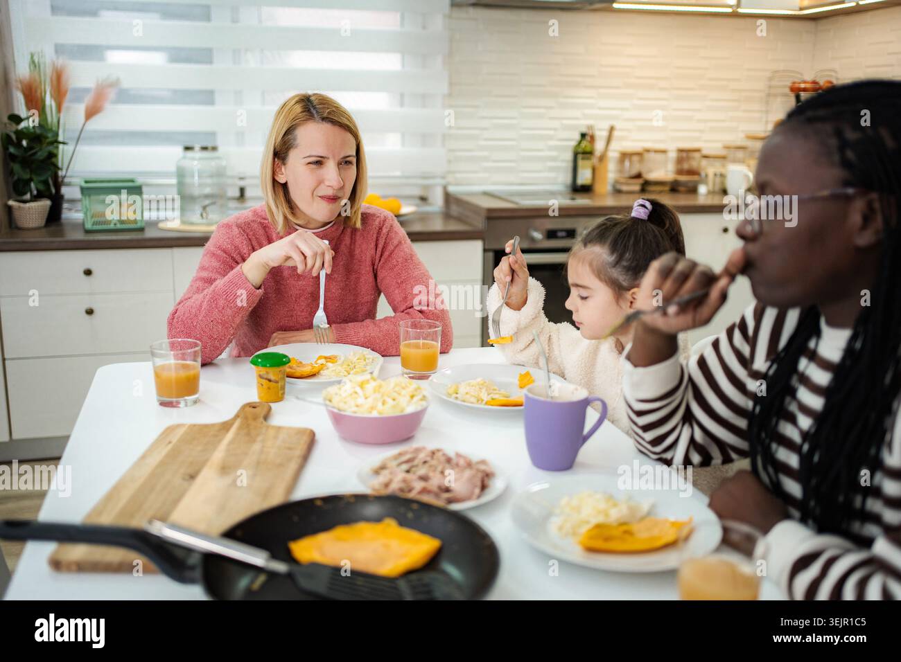 Diverse family enjoying breakfast together at home kitchen table Stock Photo