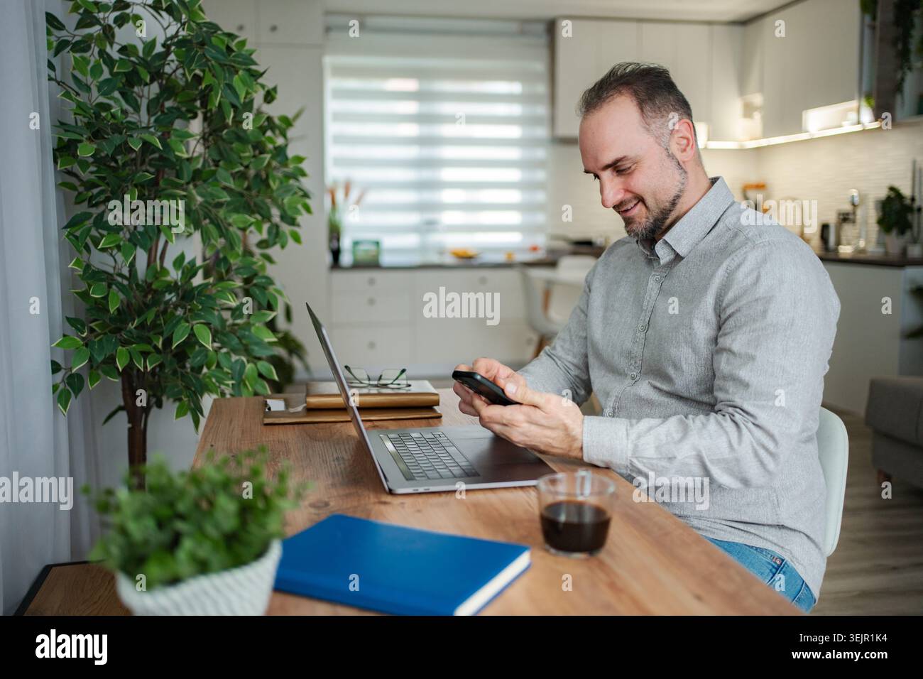 Smiling man working from home using smartphone and laptop Stock Photo