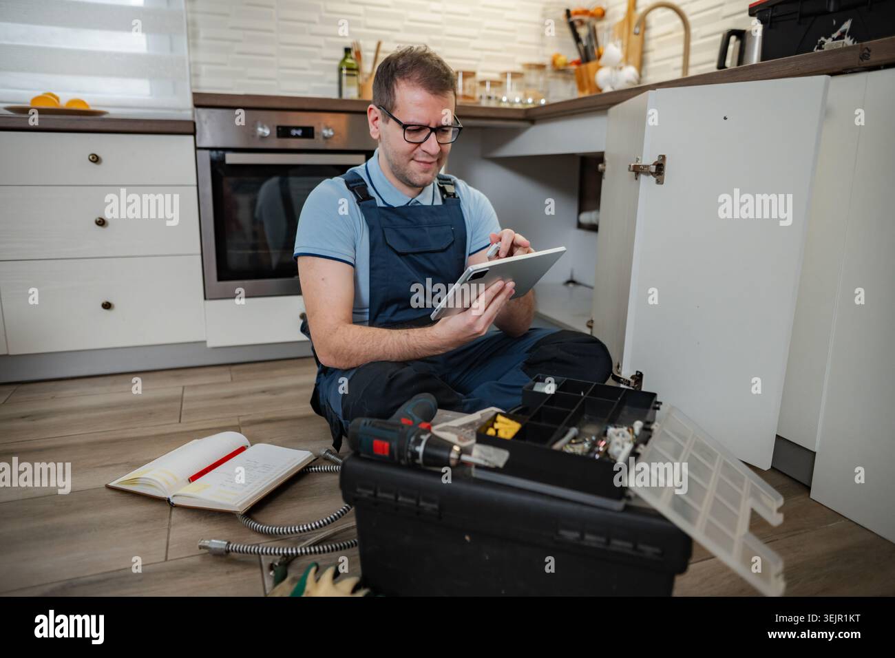 Plumber using digital tablet repairing pipe under kitchen sink Stock Photo