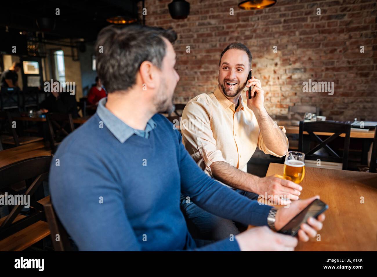 Friends socializing at pub while using technology and drinking beer Stock Photo