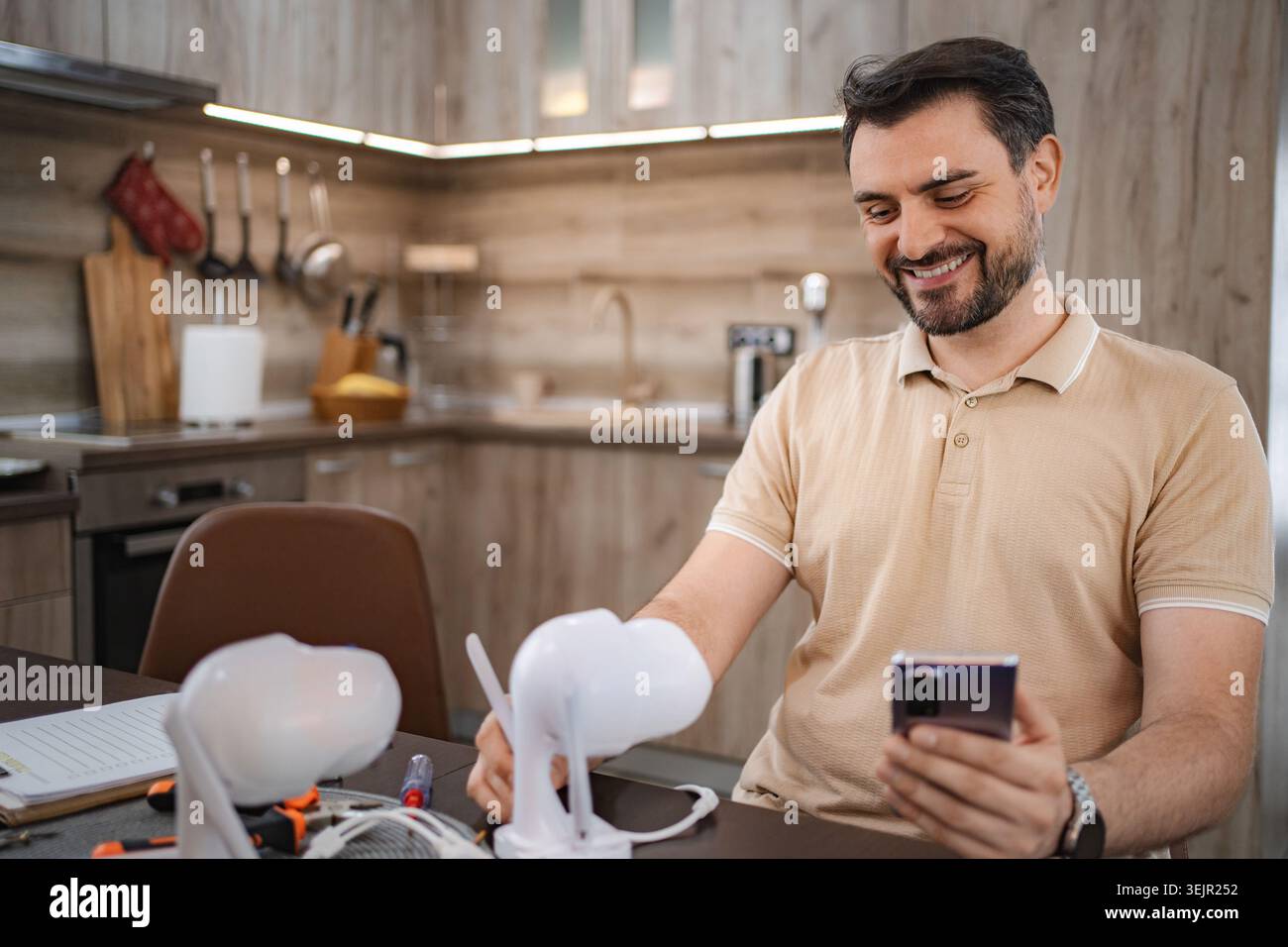 Technician smiling and using smartphone while installing smart home devices in a kitchen Stock Photo