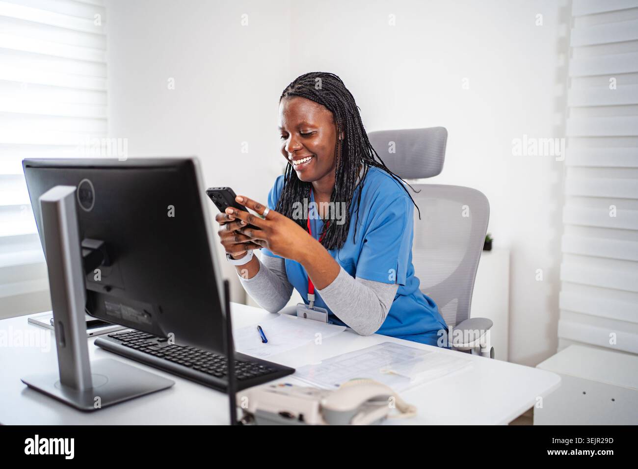 Smiling Black nurse using smartphone in office Stock Photo