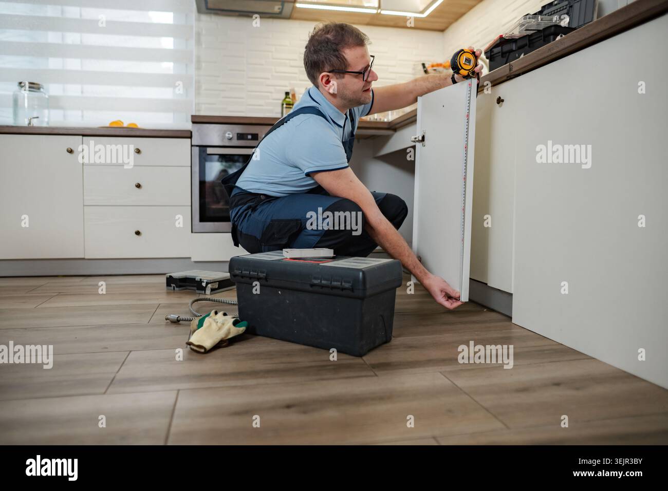 Handyman installing kitchen cabinet door, using measuring tape Stock Photo