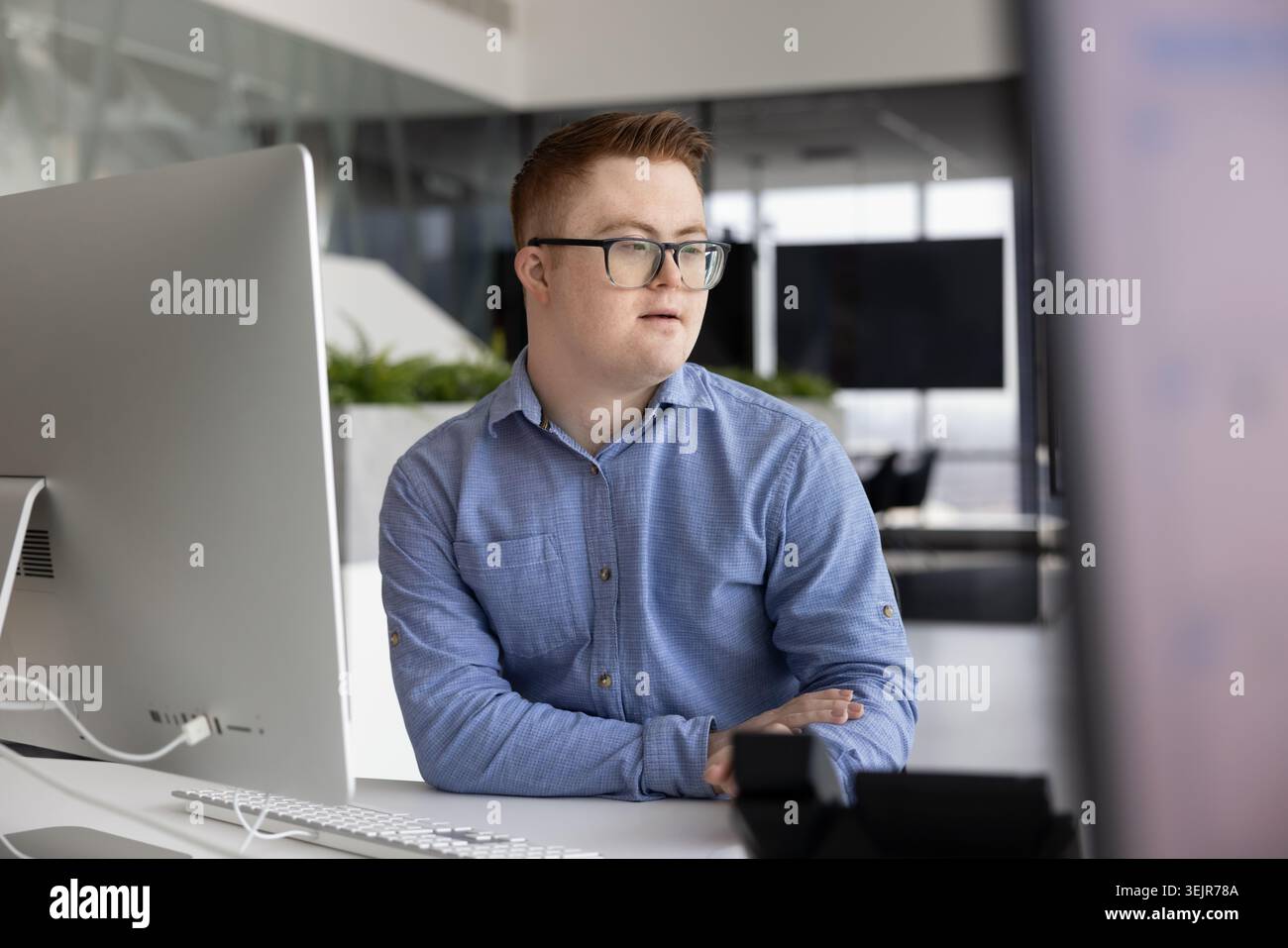 Young man with Down syndrome sitting at desk in office Stock Photo