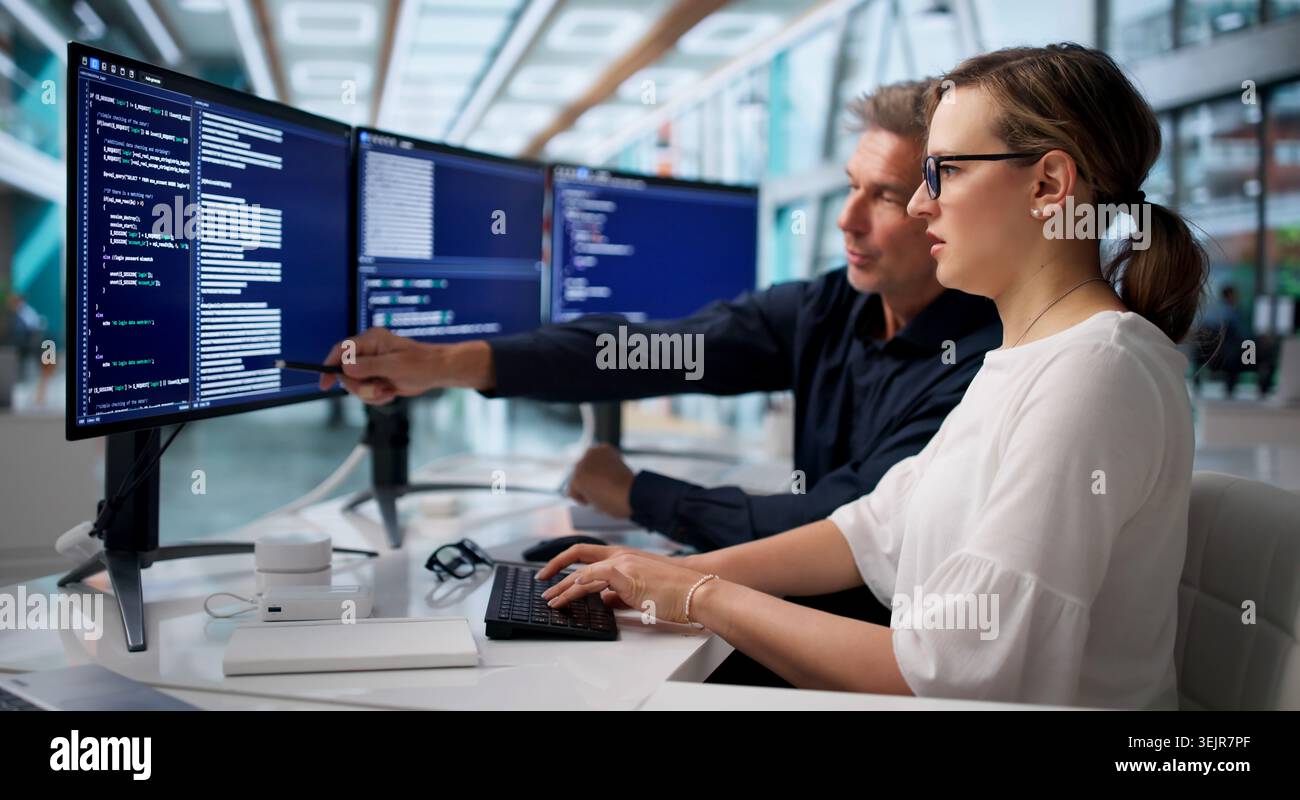 Two Software Engineers Coding Secure Systems Together At Office Desk. Stock Photo