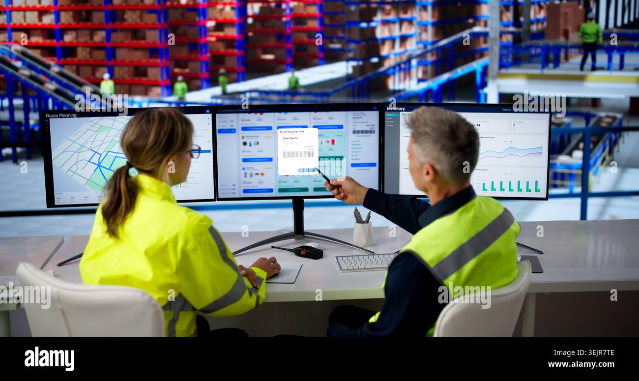 Two Workers Analyze Ecommerce Orders On Multiple Screens In Busy Warehouse. Stock Photo