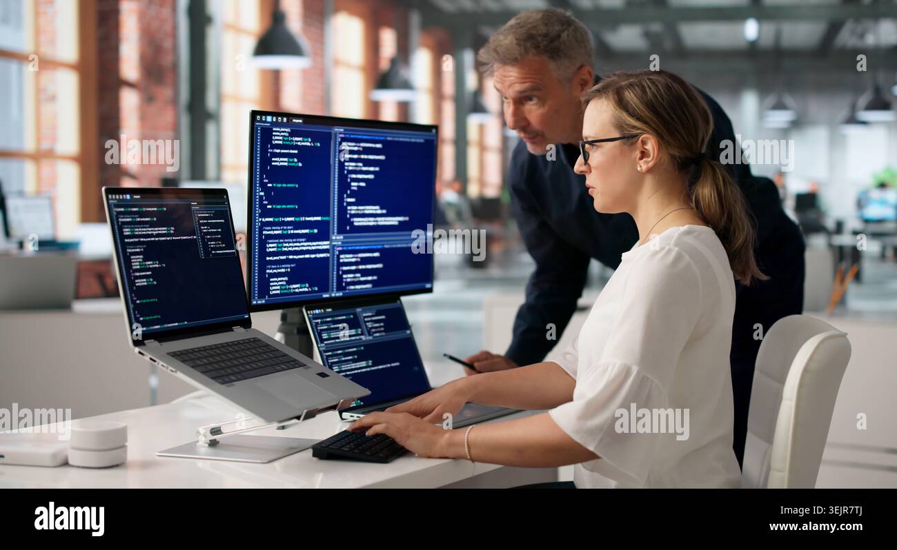 Two Software Engineers Discussing Secure Coding Solutions At Office Desk. Stock Photo