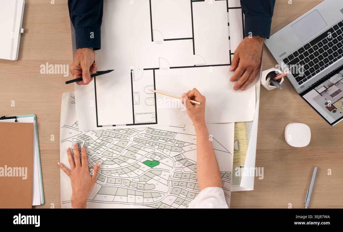 Two Urban Planners Study City Maps On Laptops, Developing New Project Plans. Stock Photo