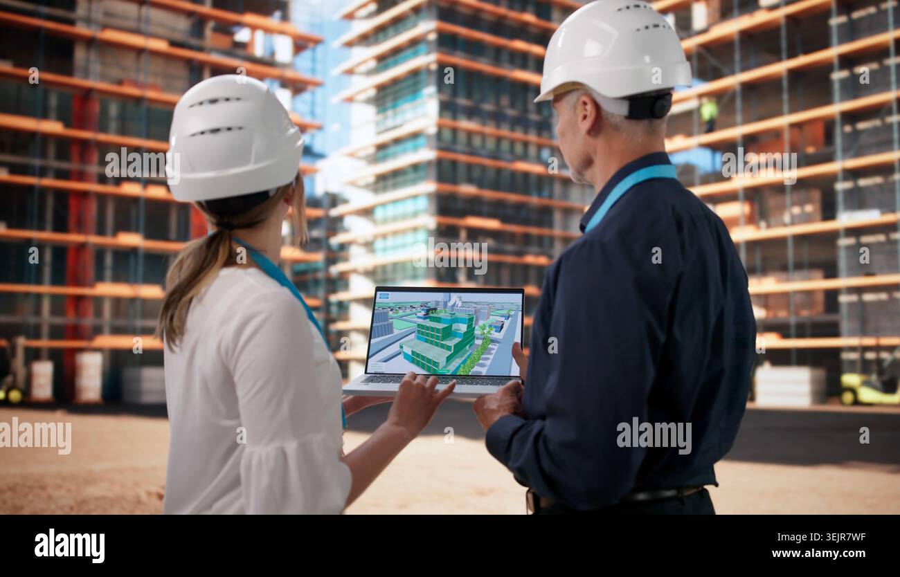 Two Architects Review BIM Model On Laptop While Planning Construction Site. Stock Photo