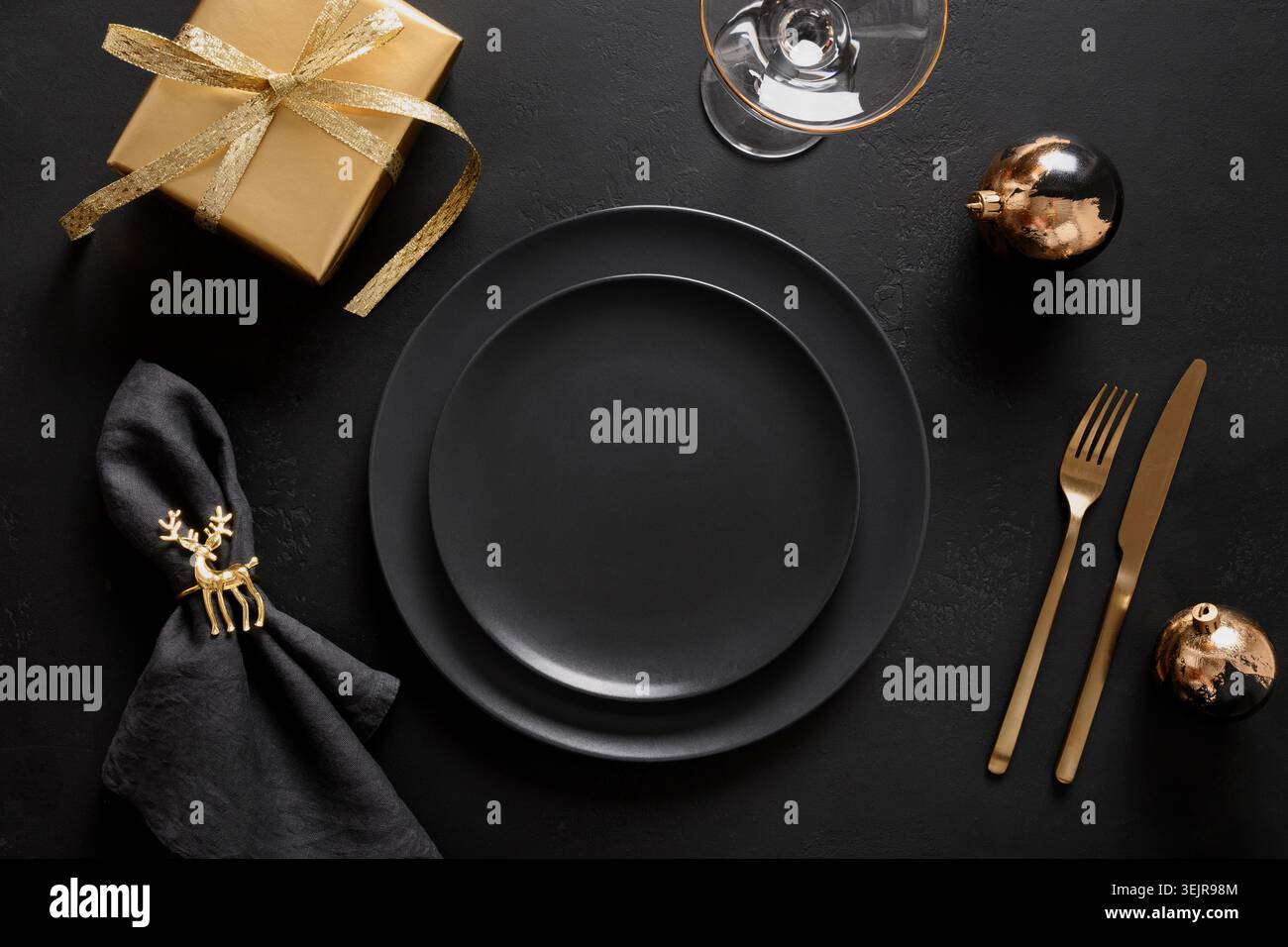 Christmas table setting with black plate and golden decorations on black. Stock Photo