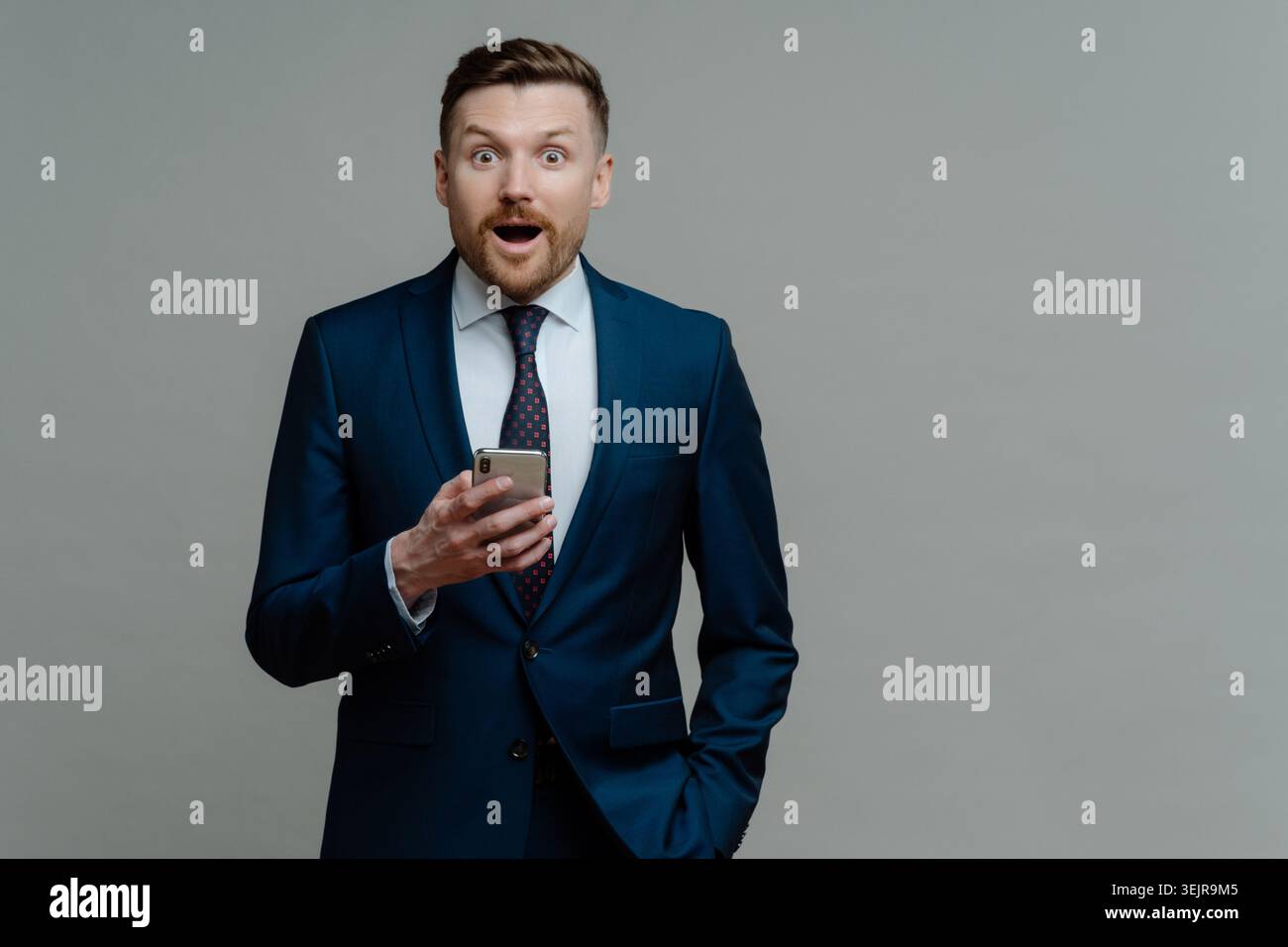 Business man checking smartphone with shocked expression on gray studio background Stock Photo