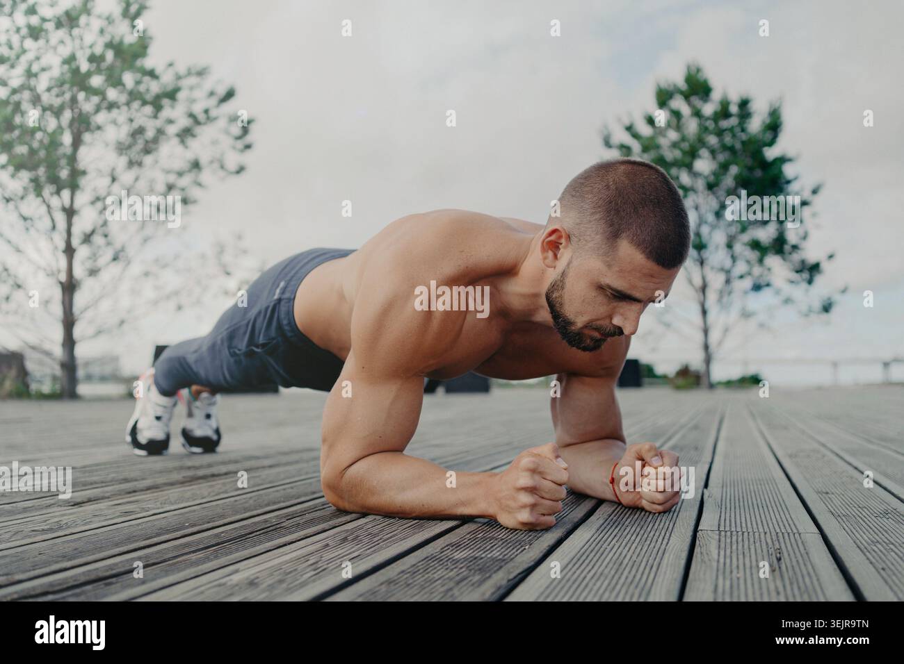 Athletic man doing plank exercise outdoors on wooden deck Stock Photo