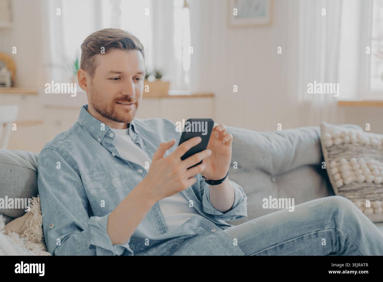 Man using smartphone while sitting on sofa at home Stock Photo