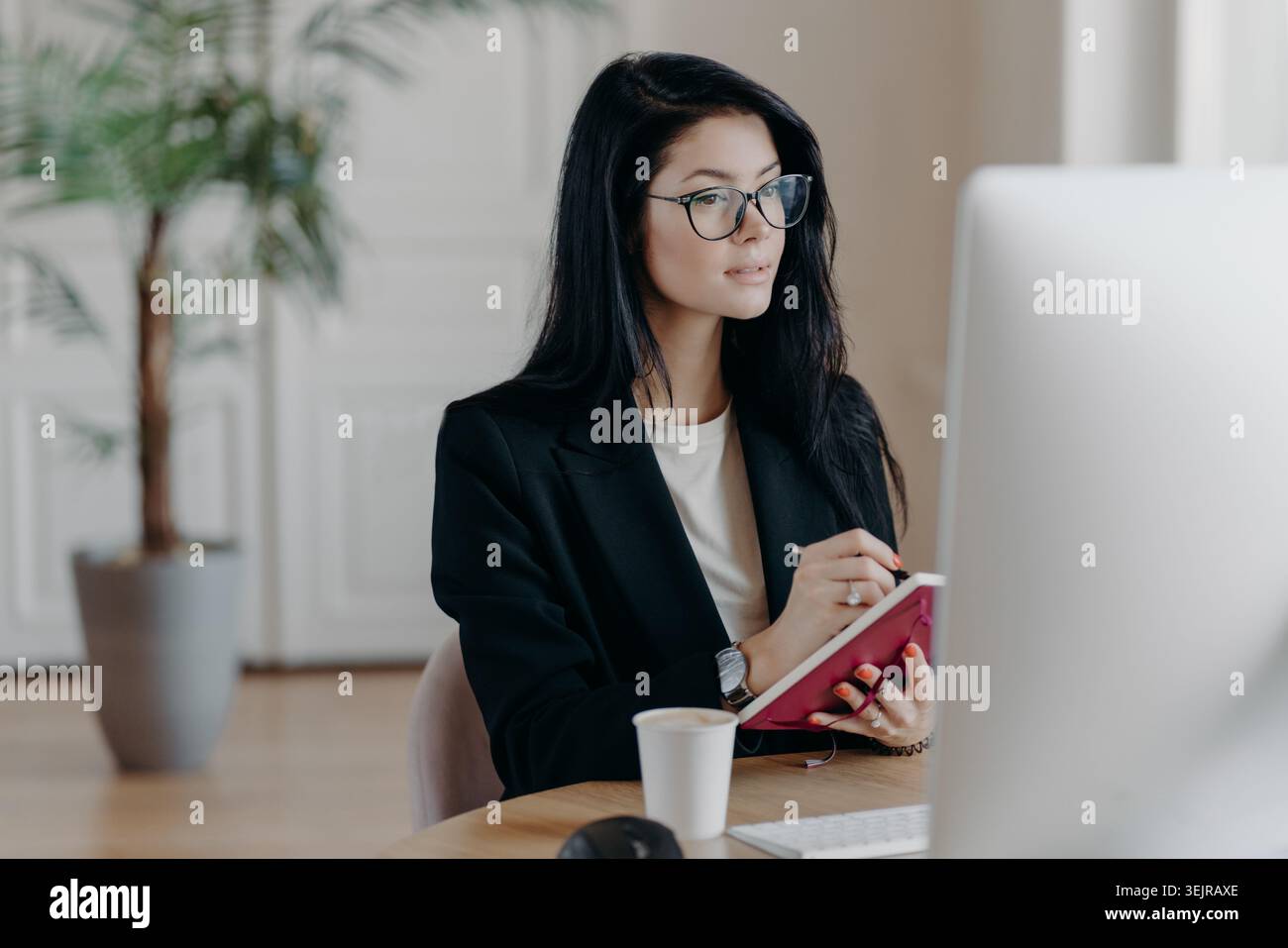 Business woman taking notes while working at computer in modern office Stock Photo