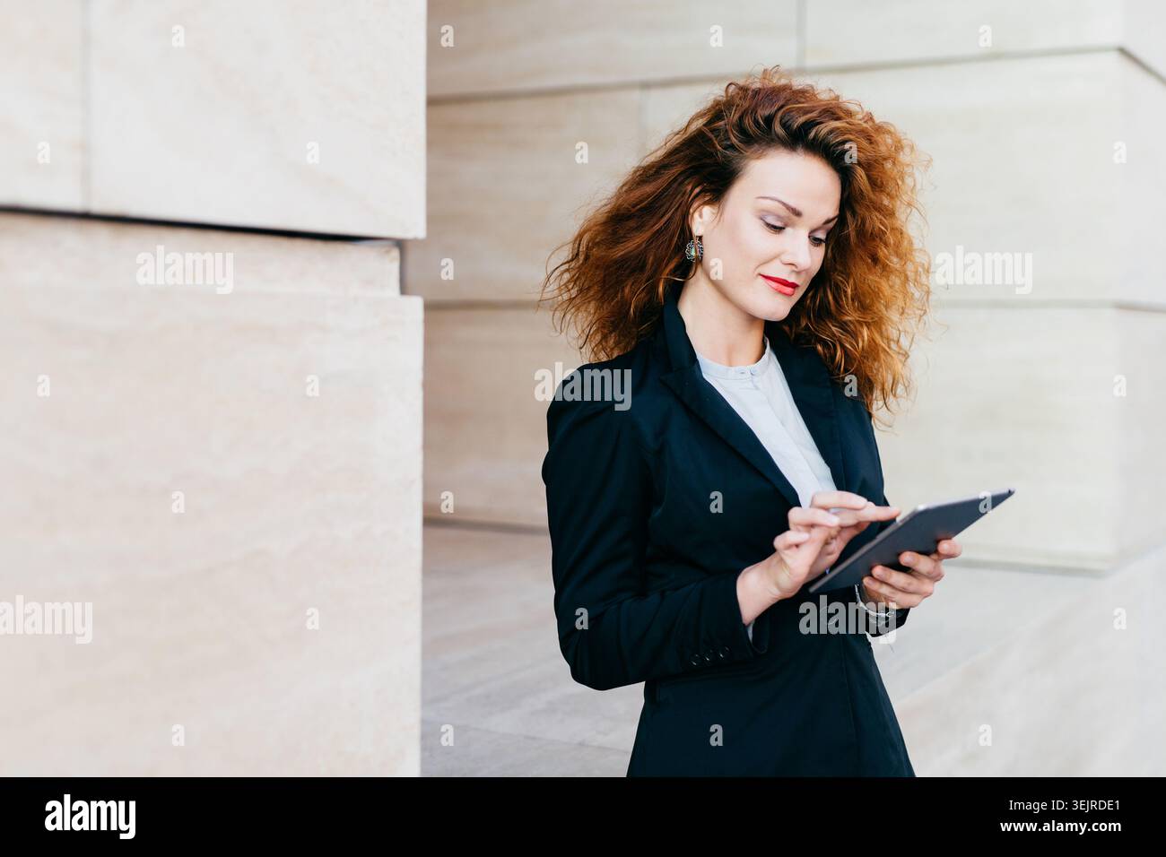 Focused Professional Woman Using Digital Tablet in Modern Office Corridor Checking Work Information on Touchscreen Stock Photo