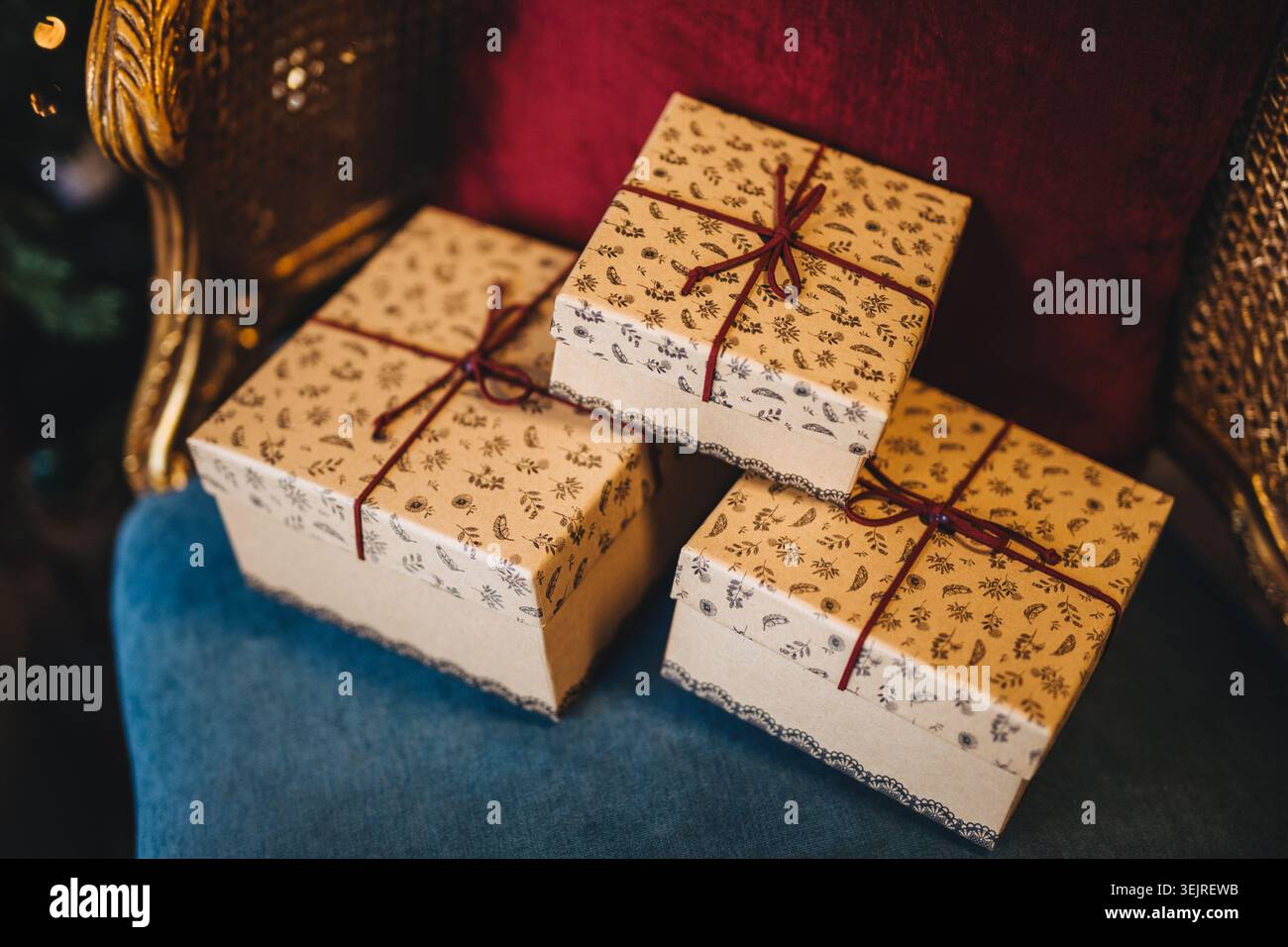 Wrapped Christmas gift boxes with red ribbons rest on vintage velvet chair Stock Photo