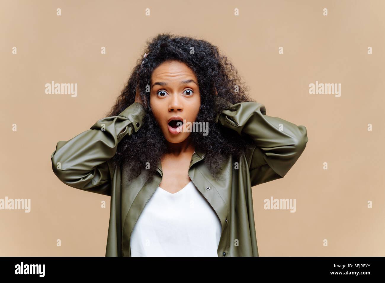 Surprised young woman holds her head while posing against beige studio wall Stock Photo