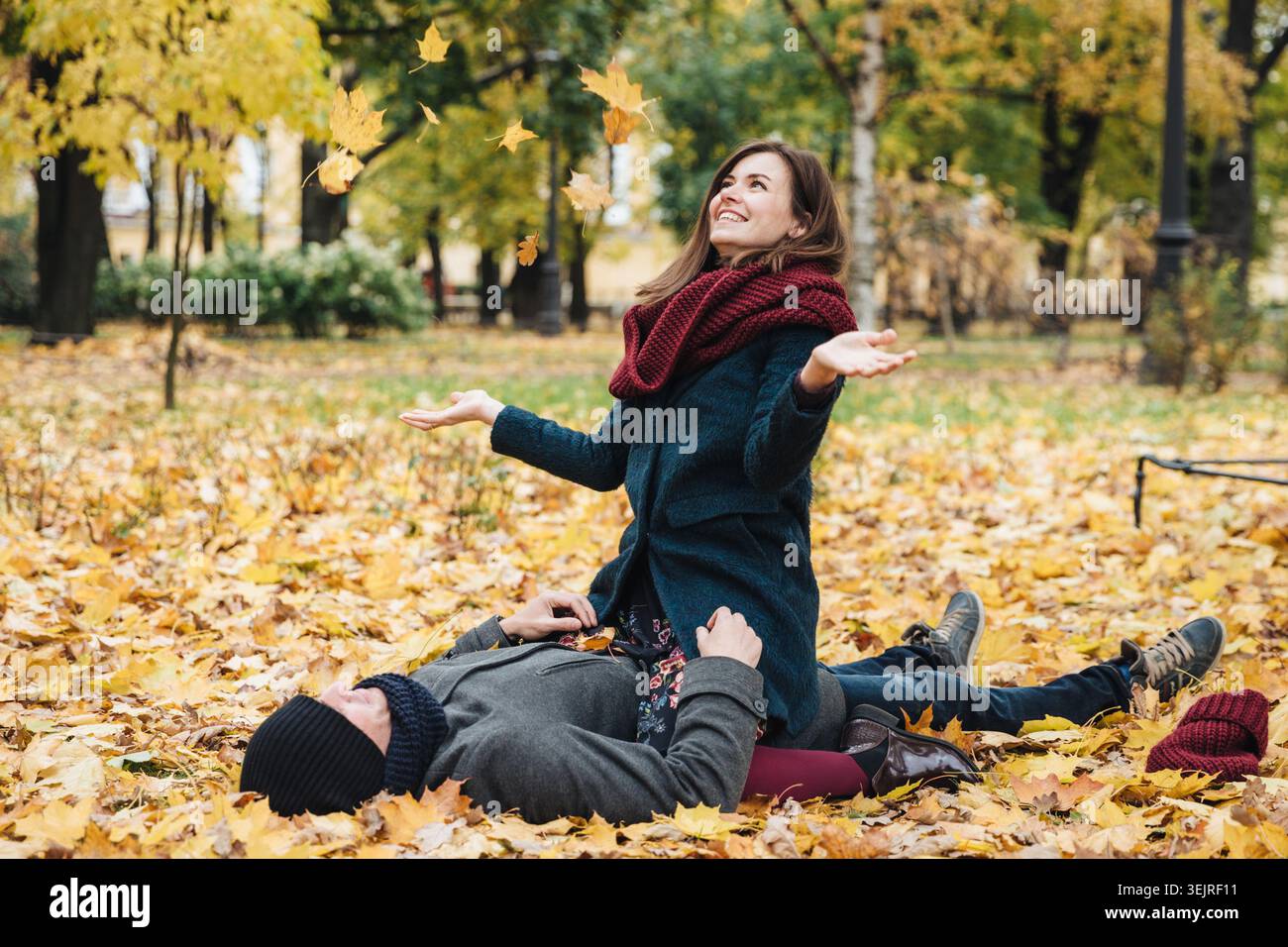 Young couple plays with fallen autumn leaves while relaxing together in city park Stock Photo