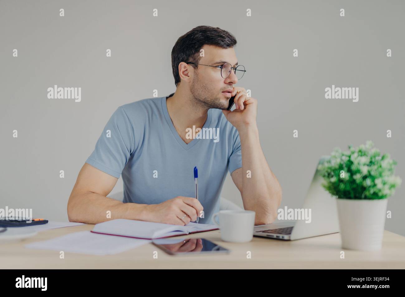 Young man writes notes beside laptop while working at home desk Stock Photo